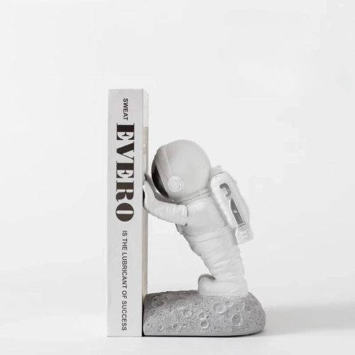 Le "serre livre découverte du monde gris" représente un astronaute blanc en combinaison spatiale sur un socle à la texture lunaire, soutenant vos livres. Cet accessoire ajoute une touche cosmique à toute étagère. Le fond est blanc uni.