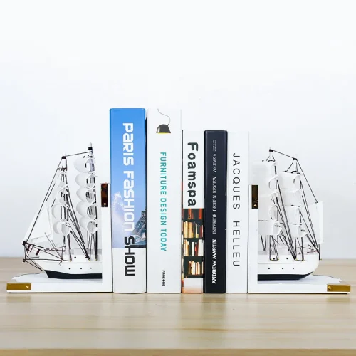 Cinq livres se tiennent debout entre deux serre-livres blancs en forme de bateaux sur une surface en bois. Idéal pour tout amateur de livres, les dos colorés présentent divers titres tandis que les serre-livres en forme de bateaux sont tournés vers l'extérieur à chaque extrémité.