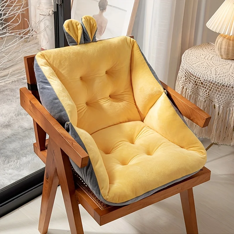 coussin de lecture sur chaise Soleil une chaise en bois avec un coussin en peluche jaune et gris avec des accents d'oreilles de lapin se trouve dans une pièce confortable avec un éclairage doux, une table recouverte de dentelle, des œuvres d'art encadrées et des étagères qui donnent une ambiance bibliothéque, ce qui en fait un accessoire de lecture idéal.