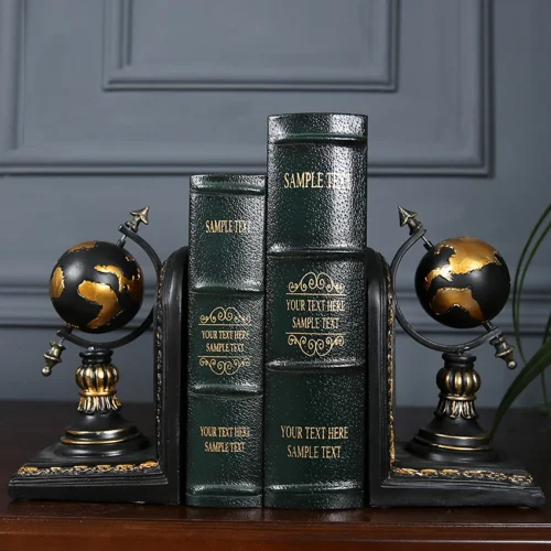 Une paire de serre-livres serre globe terrestre en noir et or soutient trois livres verts avec des détails dorés sur une surface en bois sombre, apportant l'ambiance d'une Bibliothéque sophistiquée à votre espace. Le dos des livres comporte des emplacements pour des exemples de textes.